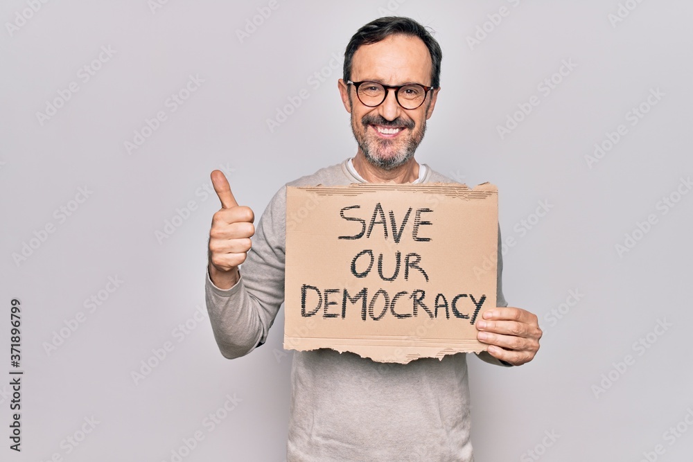 Middle age man holding banner with saver our democracy message over white background smiling happy and positive, thumb up doing excellent and approval sign Middle age man holding banner with saver our democracy message over white background smiling happy and positive, thumb up doing excellent and approval sign
