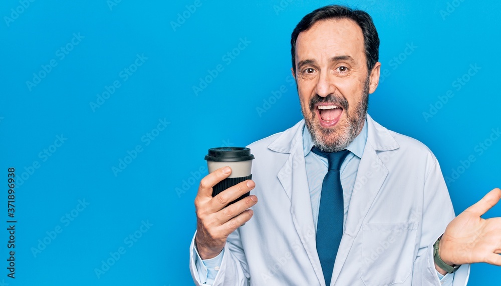Middle age handsome doctor man wearing coat drinking cup of takeaway coffee celebrating achievement with happy smile and winner expression with raised hand Middle age handsome doctor man wearing coat drinking cup of takeaway coffee celebrating achievement with happy smile and winner expression with raised hand