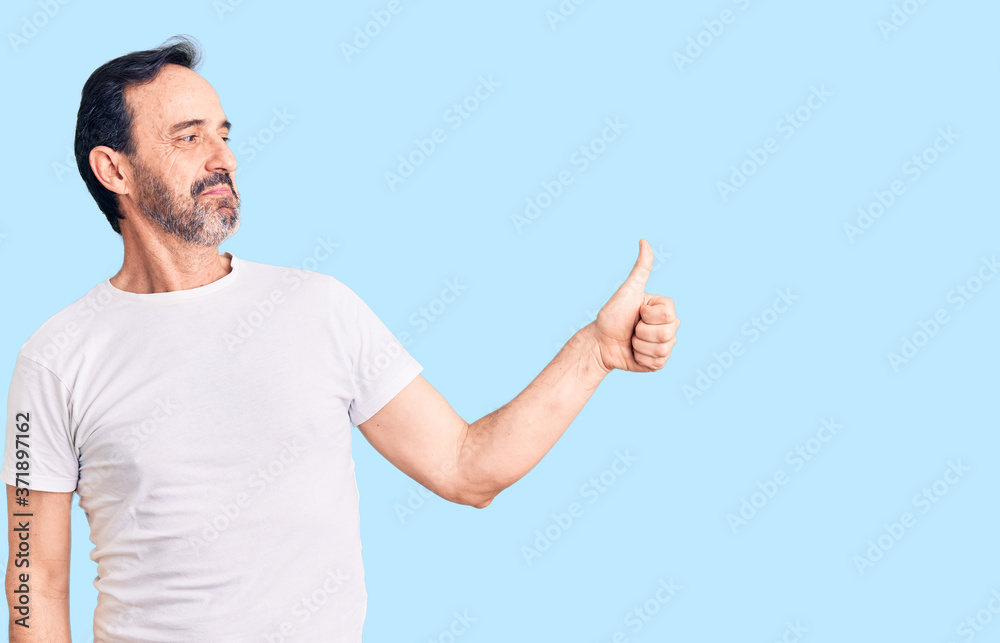 Middle age handsome man wearing casual t-shirt looking proud, smiling doing thumbs up gesture to the side Middle age handsome man wearing casual t-shirt looking proud, smiling doing thumbs up gesture to the side