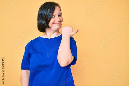 Brunette woman with down syndrome wearing casual clothes pointing thumb up to the side smiling happy with open mouth