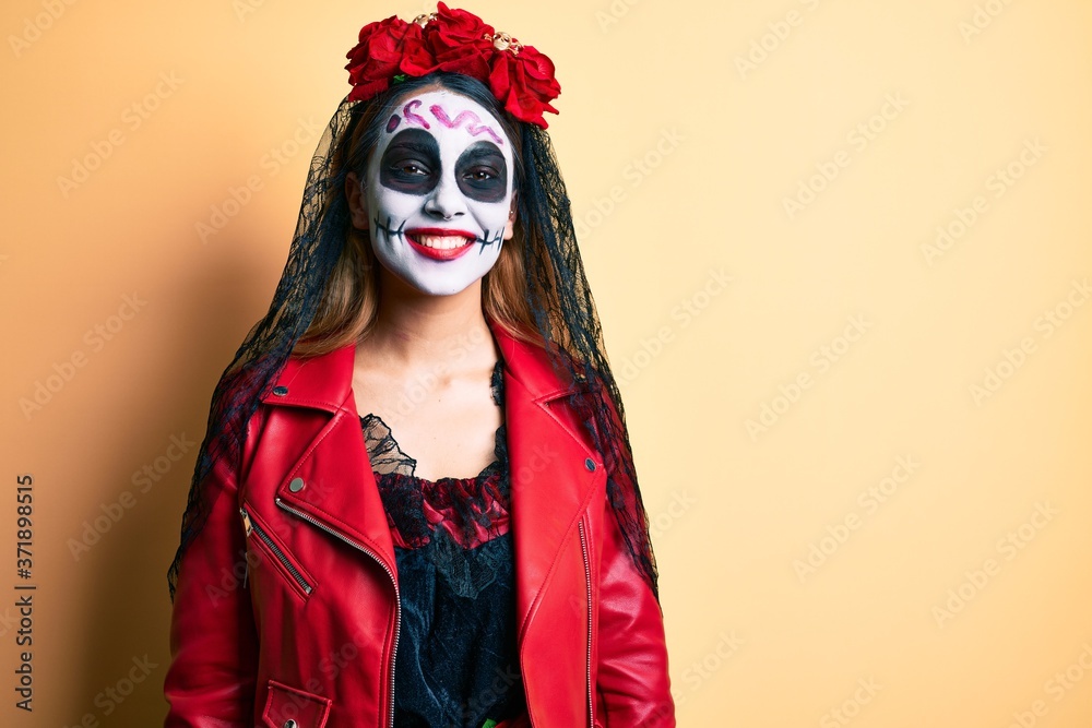 Woman wearing day of the dead costume over yellow looking positive and happy standing and smiling with a confident smile showing teeth
