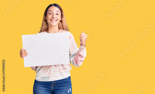 Beautiful young woman holding blank empty banner screaming proud, celebrating victory and success very excited with raised arms
