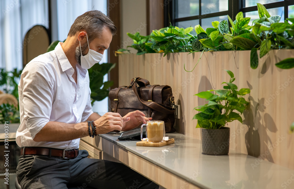 Confidence Caucasian business man typing on digital tablet with internet for online working in coffee shop. Businessman wearing face mask during protect covid-19 virus pandemic. New normal concept. Confidence Caucasian business man typing on digital tablet with internet for online working in coffee shop. Businessman wearing face mask during protect covid-19 virus pandemic. New normal concept.