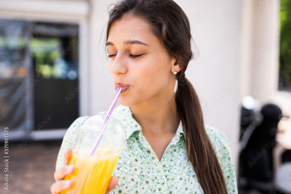 Young woman smiling and drinking cocktail with ice in plastic cup with straw