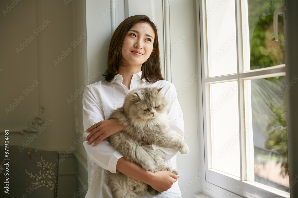 young asian woman standying by window at home holding a cat