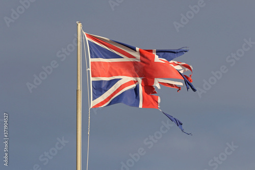 British flag or Union Jack torn and tattered flying in the winter by the sea in Italy representing the disaster of Brexit