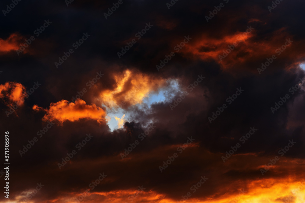 Hot flaming summer sunset. Sunset sky in red-orange tones. Dark storm clouds 