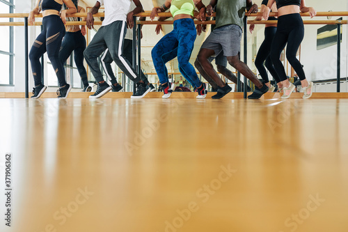 Cropped image of dancers training in class, leaning on ballet barre and standing on tiptoes