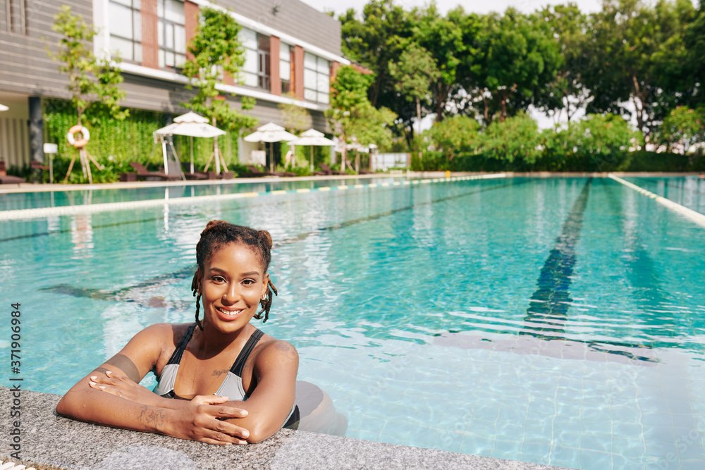 Portrait of beautiful young woman refreshing in swimming pool of spa resort on hot sunnyday