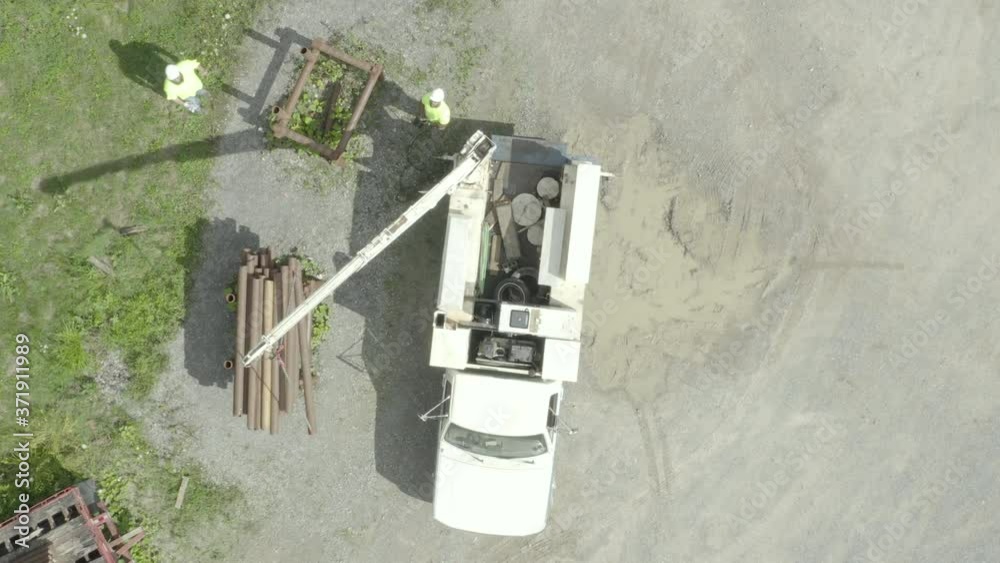 Descending drone shot of men moving pipes on a construction site with a crane truck Descending drone shot of men moving pipes on a construction site with a crane truck