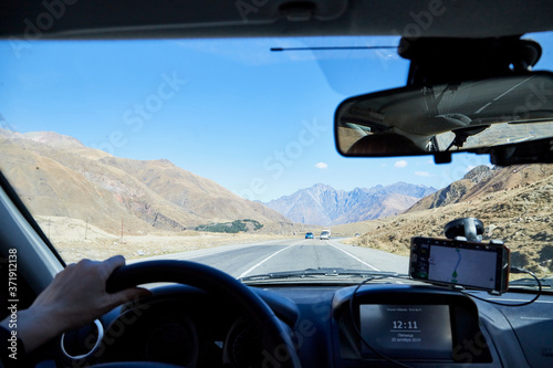 Tbilisi, Georgia - October 25, 2019: Car vindow, hand of woman on steering wheel and view to the road and autumn mountain landscape photo