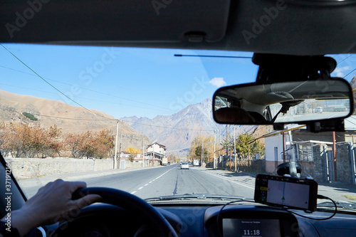 Fototapeta Naklejka Na Ścianę i Meble -  Tbilisi, Georgia - October 25, 2019: Car vindow, hand of woman on steering wheel and view to the road and autumn mountain landscape