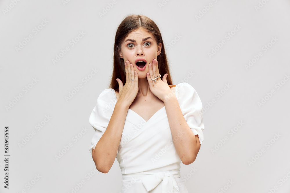 Surprised woman holding her face with open mouth white dress gray background Surprised woman holding her face with open mouth white dress gray background