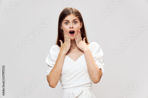 Surprised woman holding her face with open mouth white dress gray background