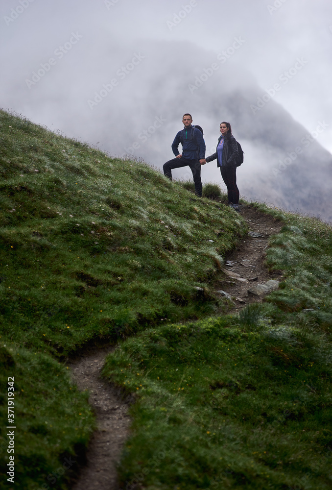 Full length of young woman and boyfriend standing on hillside path and holding hands. Loving couple hiking together in mountains. Concept of hiking, traveling and relationships.