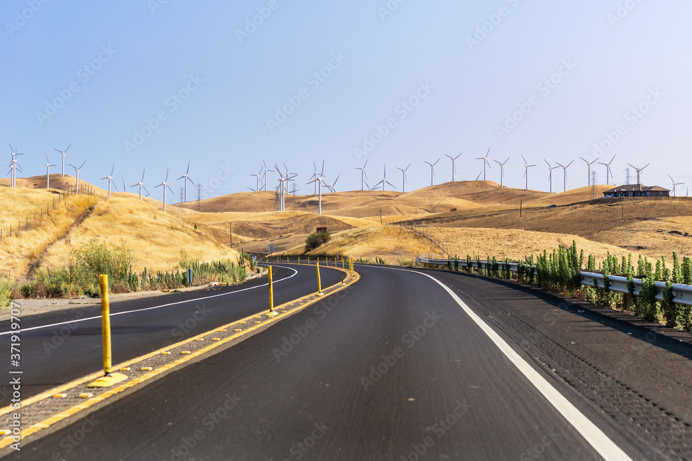 Fototapeta premium Highway crossing the hills and valleys of Alameda County close to Altamont Pass; Wind turbines visible on the golden hills; San Francisco Bay Area, California