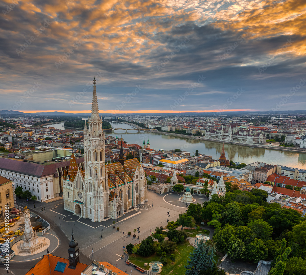 Fototapeta premium Budapest, Hungary - Aerial drone view of the beautiful Matthias Church in the morning with Fisherman's Bastion (Halaszbastya) and Parliament of Hungary at background. Colorful clouds at sunrise