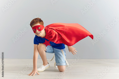 Cheerful boy in superhero costume ready to fight evil on grey background. Positive child pretending to be superman