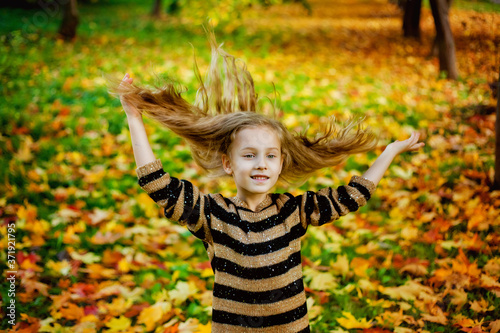 Portrait of a little girl in a striped sweater, tossing her hair in an autumn Park among yellow maple leaves.