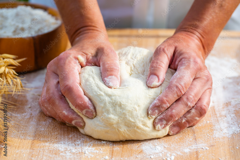 Woman hands kneading dough on the wooden board.