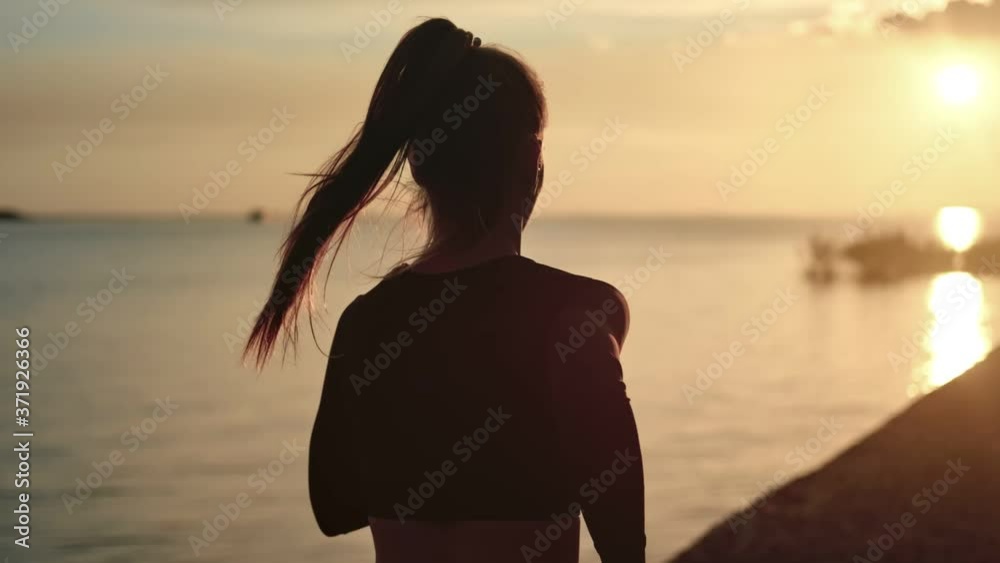 Athletic woman with waving hair running on beach at dramatic sun. Medium shot on RED camera
