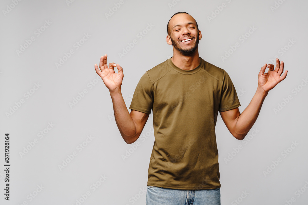 Stress relief techniques concept - happy young african-american man meditating with eyes closed over grey background Stress relief techniques concept - happy young african-american man meditating with eyes closed over grey background
