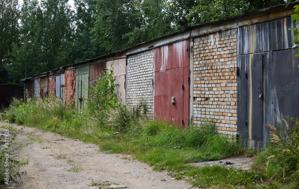 A row of old brick garages with metal gates on a dirt road