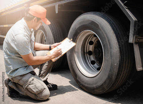Maintenance and Vehicle inspection. A truck mechanic, driver holding clipboard, his is checking safety a truck wheels and tires.