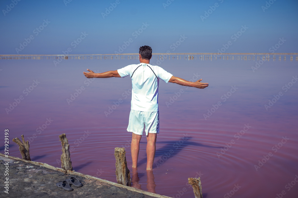 Brunet man relaxing on pink salty Sivash Lake near Azov Sea, colored by microalgae Dunaliella salina, enriching water of the lake by beta-carotene