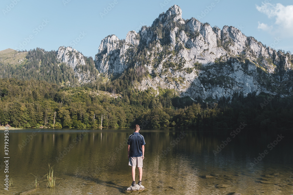 Young man standing on rock in Laudachsee with alps mountain. Summer Austria landscape Young man standing on rock in Laudachsee with alps mountain. Summer Austria landscape