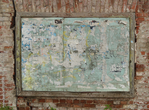 Old dirty wooden board with scraps of advertisements on a vintage brick wall.