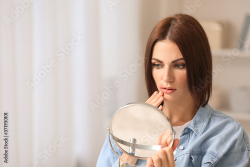 Young woman with cold sore looking in mirror at home photo