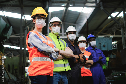 Industrial woman engineer wearing hygiene face mask and hardhat with workers in factory,new normal of industry for protection covid-19 pandemic.