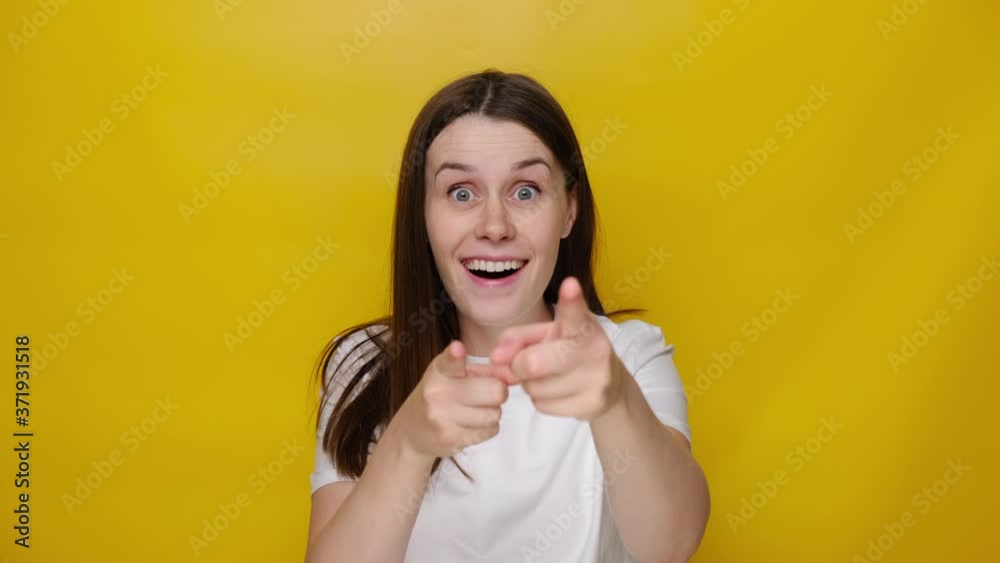 Amazed funny millennial young woman pointing finger to camera, looking big eyes surprised expression, shocked by sudden success, wears t-shirt, isolated on yellow studio background. Wow, hey you! 