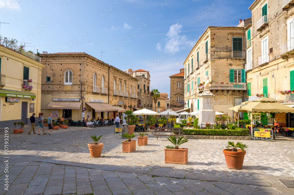 Tropea, Italy - May 9, 2018: Streets of town with cafes and restaurants, buildings with balconies, vases with flowers and shutter windows, blue sky with clouds on backgrond, Calabria