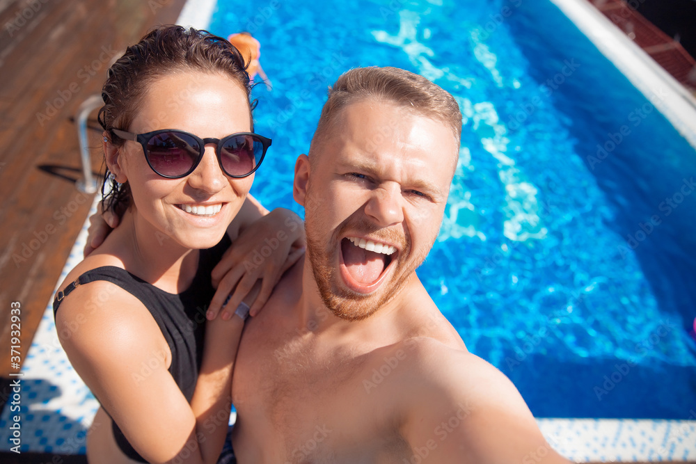 Happy loving couple Caucasian man and woman hugging and making selfie photo on background of pool. Smile and tanned skin summer time Happy loving couple Caucasian man and woman hugging and making selfie photo on background of pool. Smile and tanned skin summer time