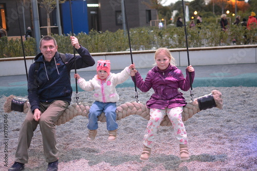 Dad and his daughters sit on a swing at the site  Salyut  in Gorky Park in Moscow.