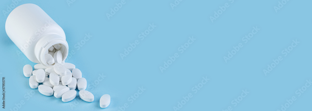 Pills spilling out of white bottle on blue background with copy space. Pharmaceutical medicament, cure in container for health. Medicine concept. Long wide banner
