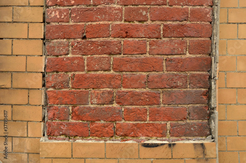 Collapsed cracked decorative imitation brick wall cladding on an old red brick wall