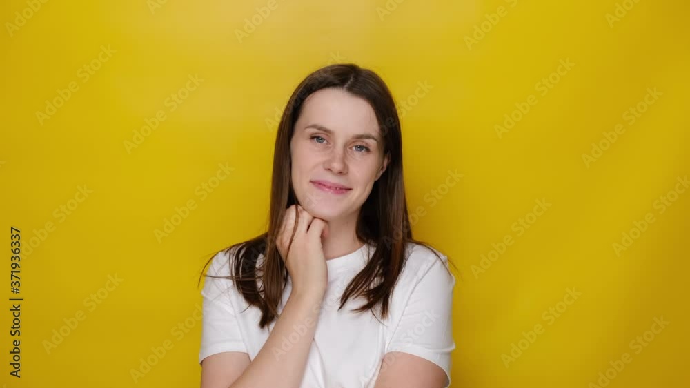 Cute young woman smiling looking at camera posing on yellow studio background. Charming girl smile, wears white t-shirt, female casting for tv commercial ad, university student portrait concept Cute young woman smiling looking at camera posing on yellow studio background. Charming girl smile, wears white t-shirt, female casting for tv commercial ad, university student portrait concept