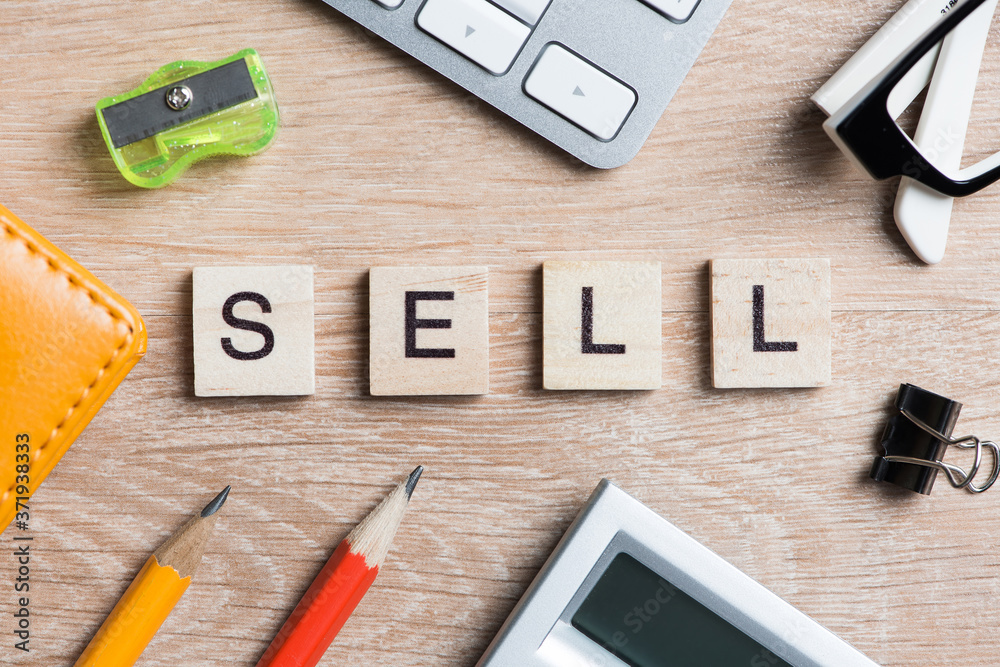 Office stuff and SELL word spelled with wooden blocks on workplace table Office stuff and SELL word spelled with wooden blocks on workplace table