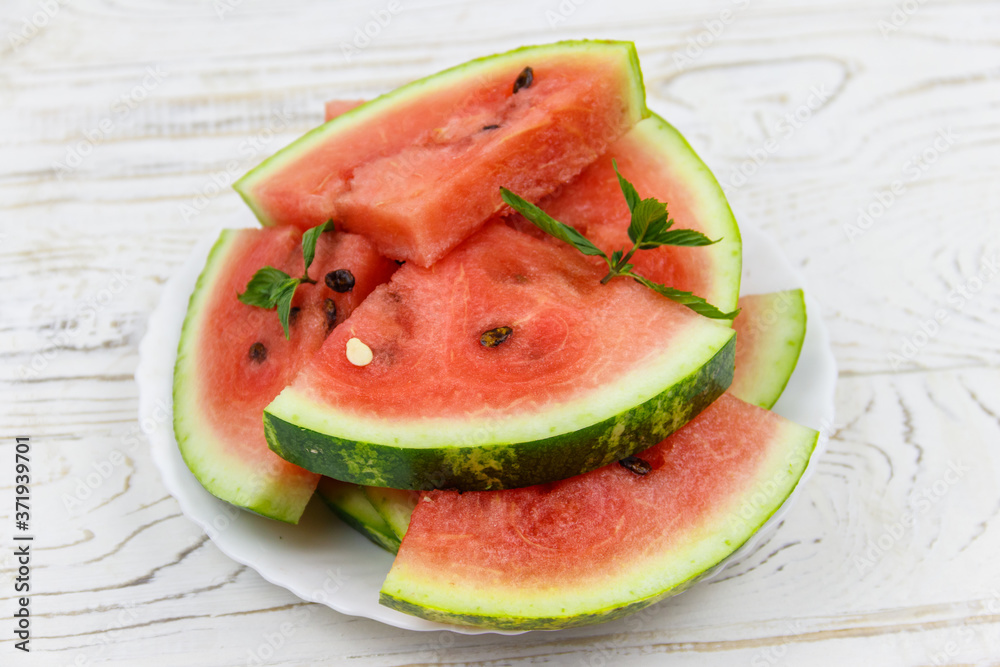 Fresh ripe sliced watermelon in white plate on a white wooden table