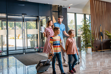 Smiling family of four in the hotel lobby check in at the reception for vacation.