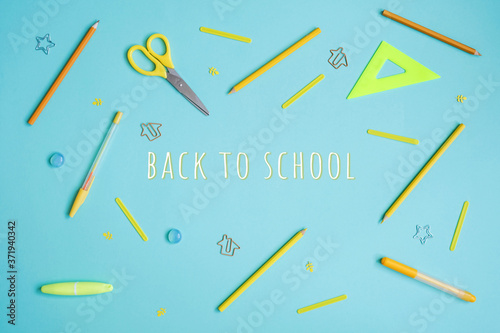 Stationery on blue. Bright stylish flat lay. Different yellow tools with Back to School lettering in centre.