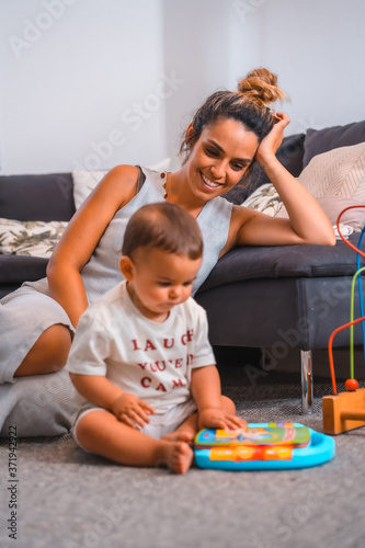 Young Caucasian mother with her son sitting on the floor next to the black sofa. Teleworking and caring for your child, a new normal after the coronavirus pandemic, covid-19. Watching the child play