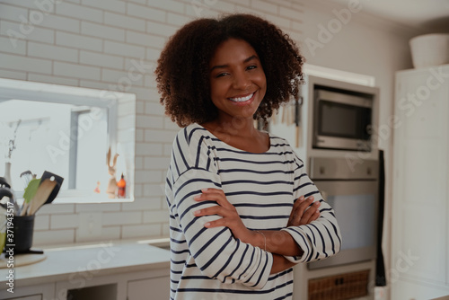 Portrait of cheerful young african woman standing in modern kitchen with folded arms looking at camera