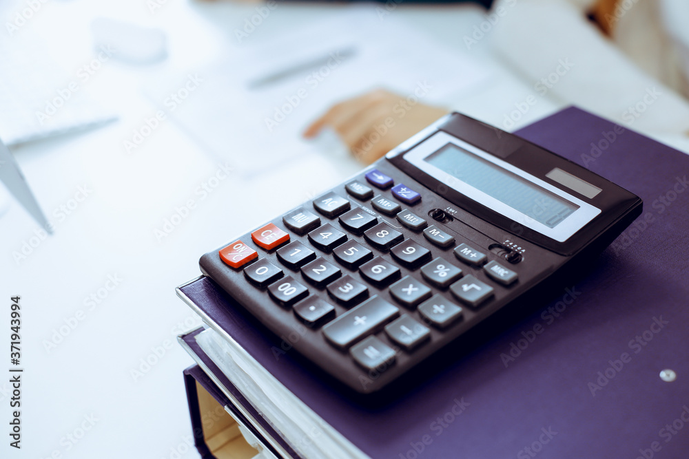 Calculator and binders with papers are waiting to be processed by business woman or bookkeeper working at the desk in office back in blur. Internal Audit and tax concept Calculator and binders with papers are waiting to be processed by business woman or bookkeeper working at the desk in office back in blur. Internal Audit and tax concept