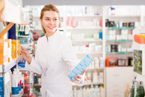 Young friendly woman pharmacist offering reliable medicine in pharmaceutical shop