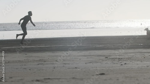 Silhouette of man running on a beach pretending to throw something at stray dog to shoo away slow motion photo