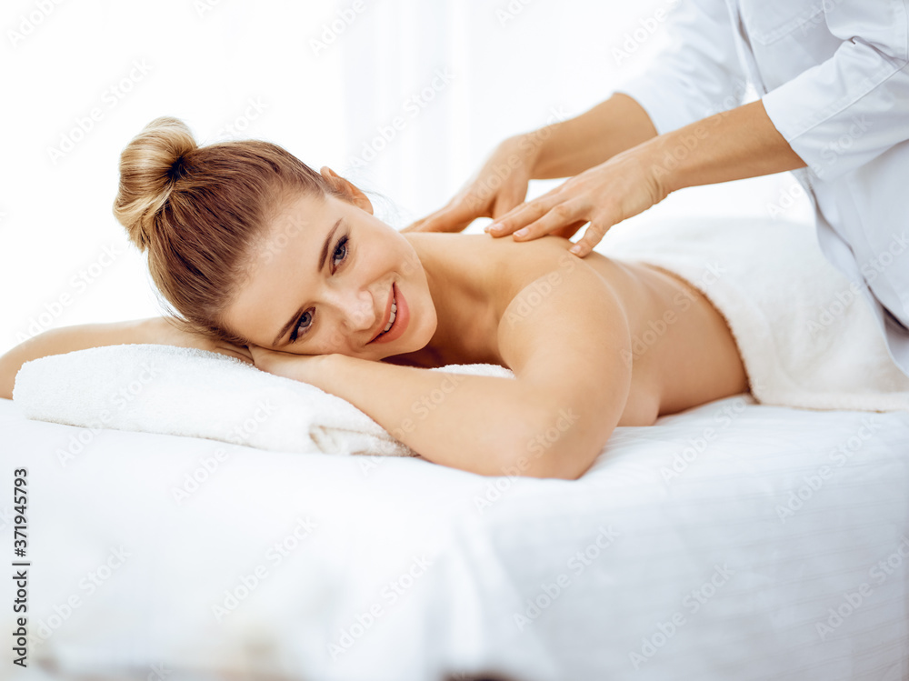 Young and blonde woman enjoying massage of back in spa salon. Beauty concept Young and blonde woman enjoying massage of back in spa salon. Beauty concept